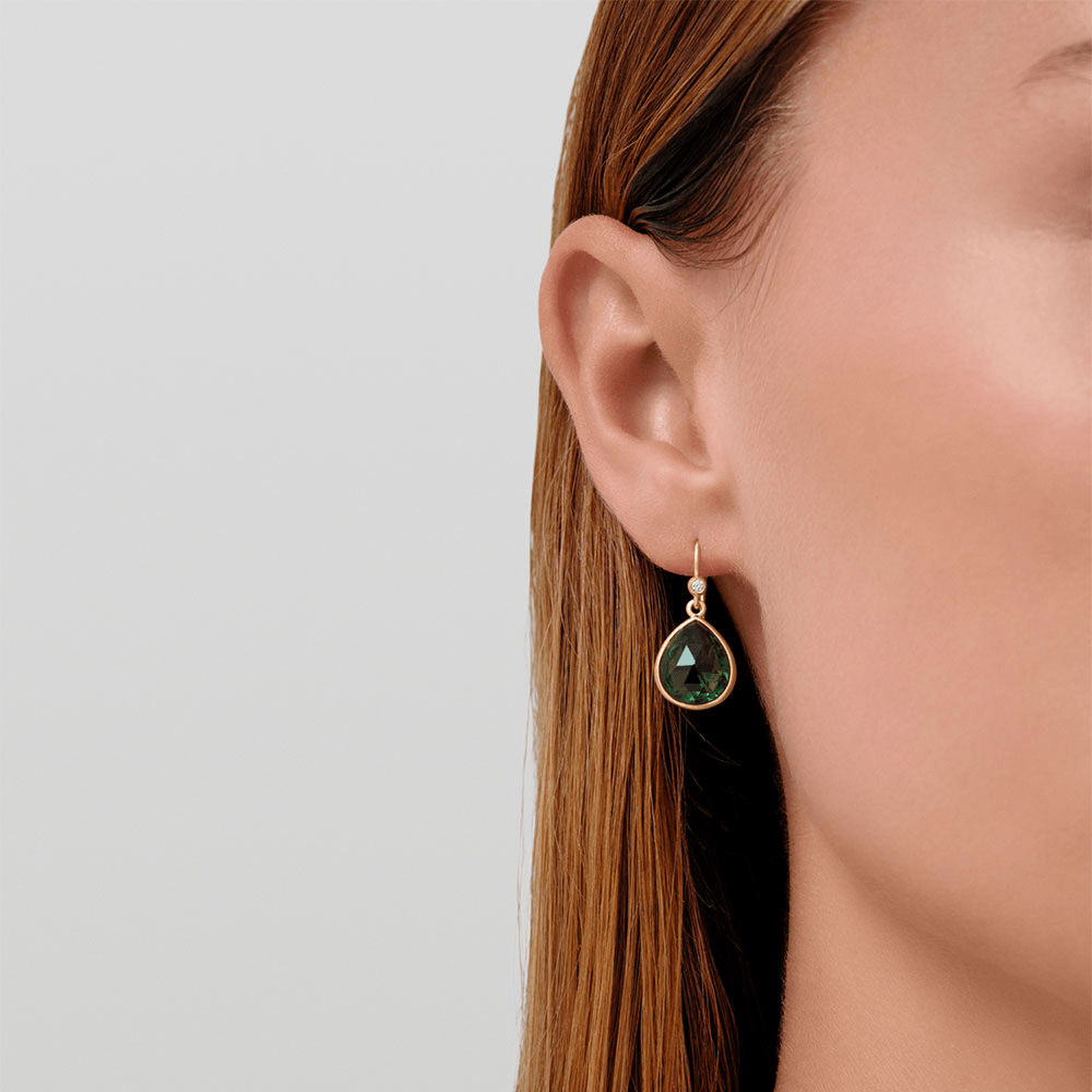 Model bærer Lea Earrings i forgyldt sølv med grøn pear-slebet krystal, tæt på øret