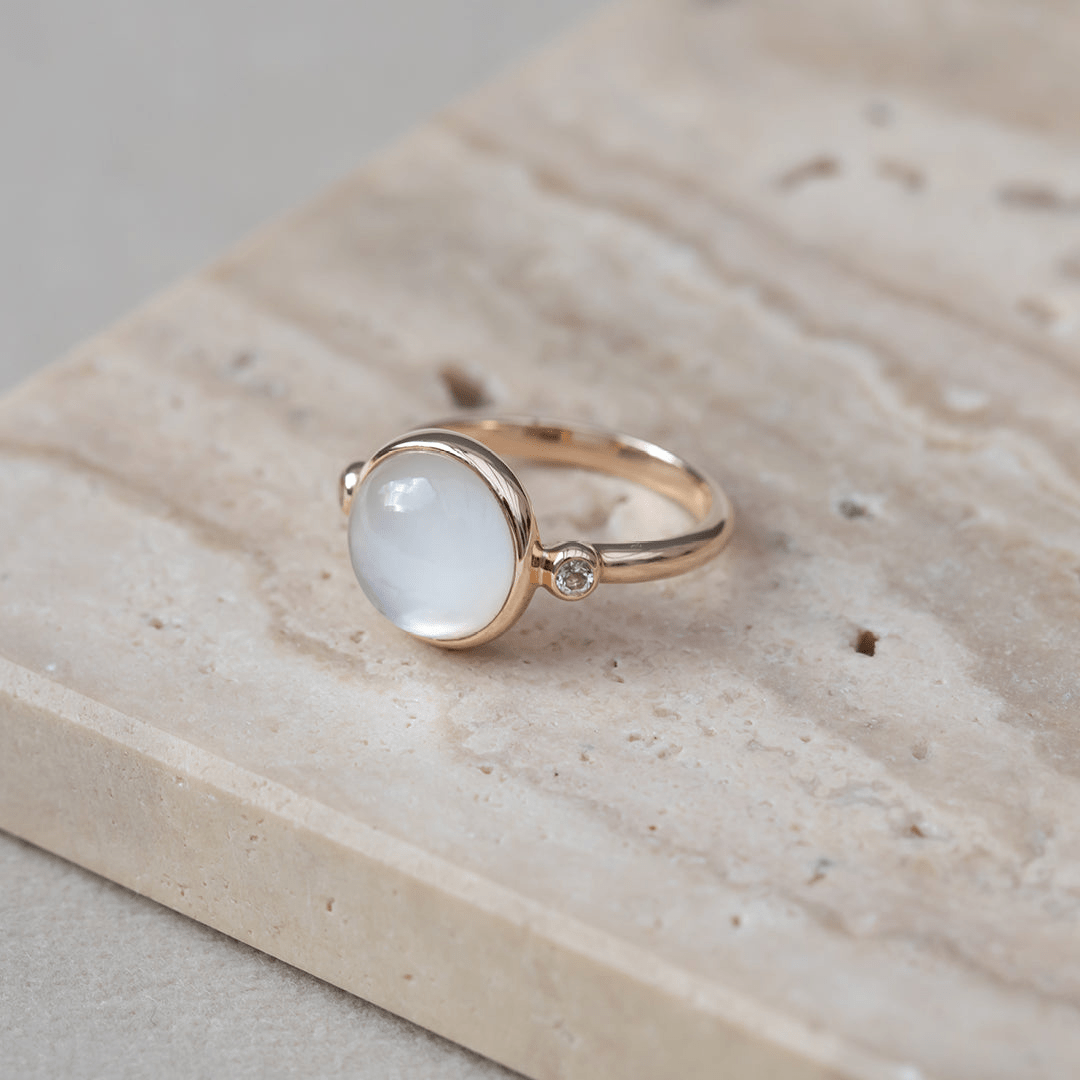 Carla Ring i guld med hvid cabochon-slebet sten, foto på stensokkel