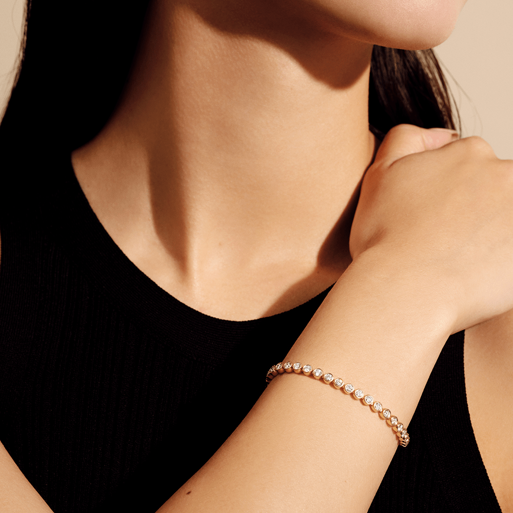 Close-up af Lumi armbånd i guld på håndleddet med diamantbesatte led
