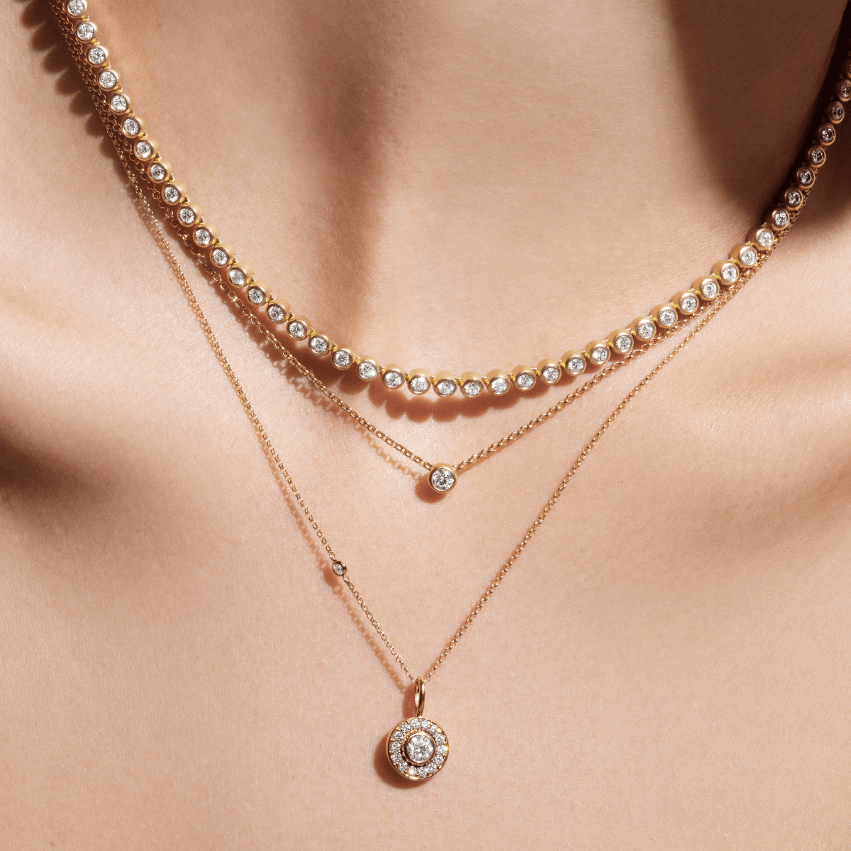 Model bærer flere lagdelte halskæder, heriblandt Heritage Pendant, sammen med en diamantbesat tennishalskæde og andre vedhæng