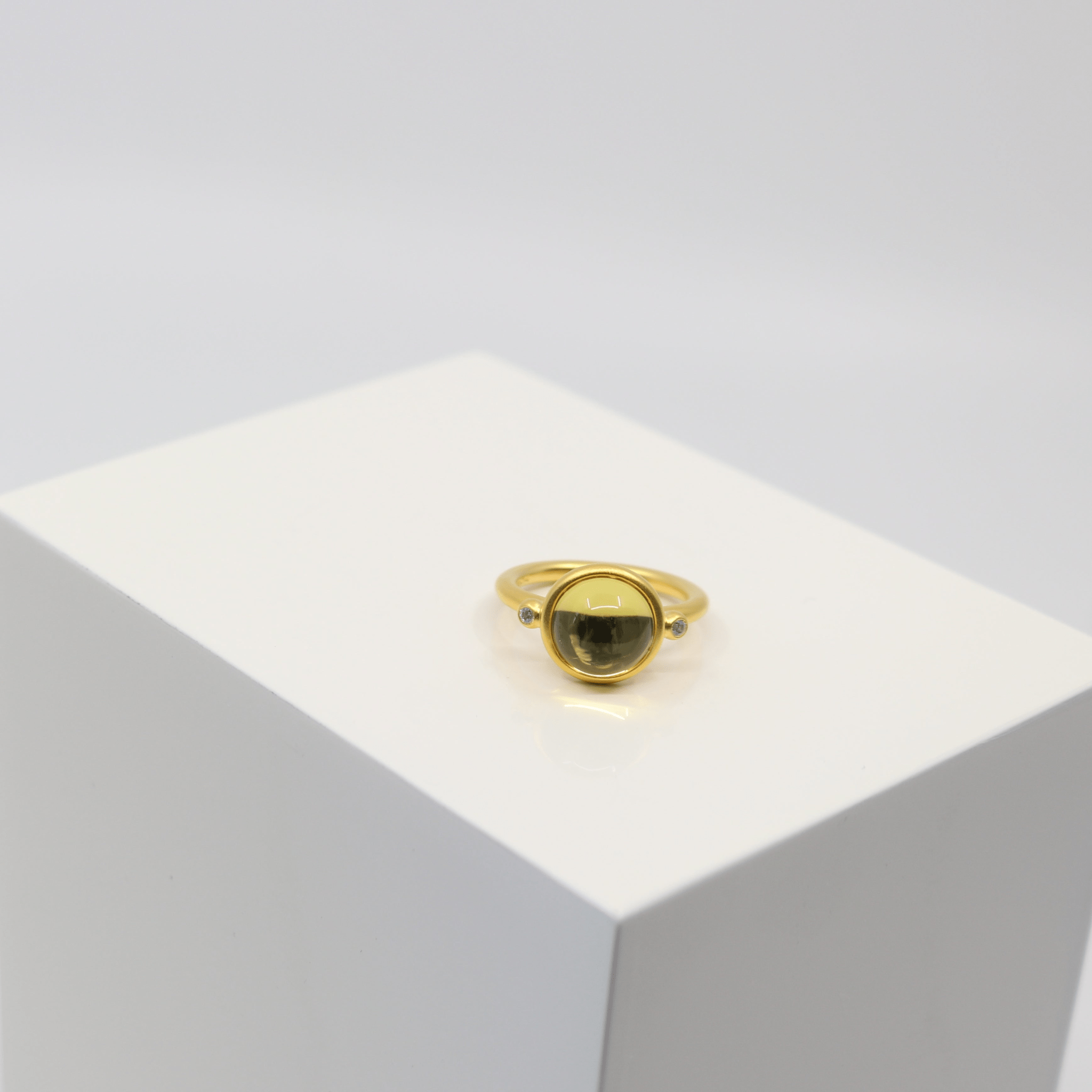 Prime Ring i sandblæst guld med olivengul cabochon-krystal, stylet på hvid sokkel