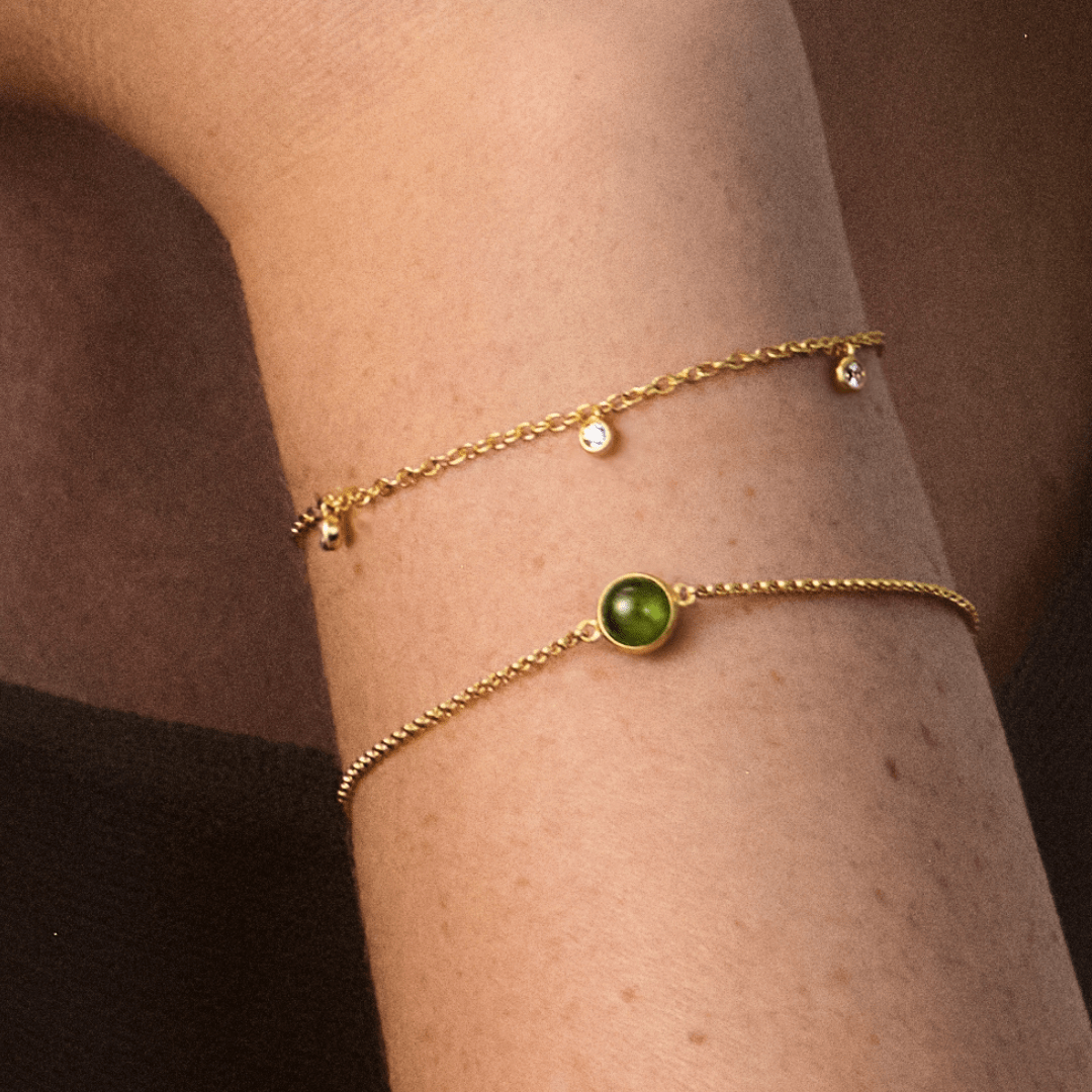 Primini armbånd med grøn cabochon-krystal båret på håndled, lagdelt med et tyndt sølvarmbånd med to klare sten
