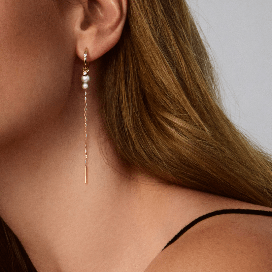Model bærer guld hoop-ørering med perle og lang kædedrop fra Eden looket