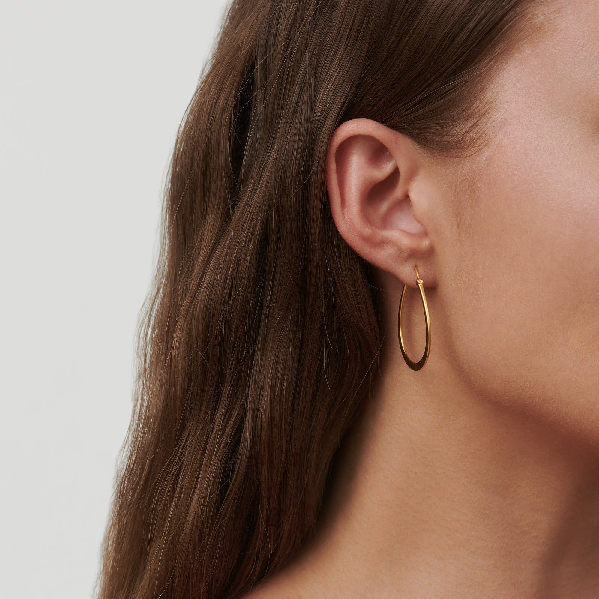 Model bærer Classic Pear Hoop øreringe i mat guld, set ved hals og øre