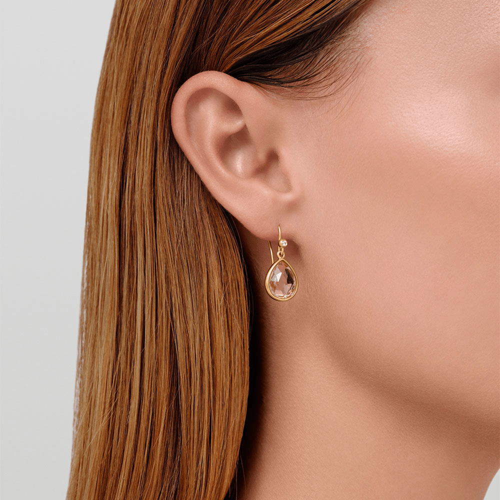 Model bærer Lea Earrings i forgyldt sølv med lyserød pear-slebet krystal, tæt på øret