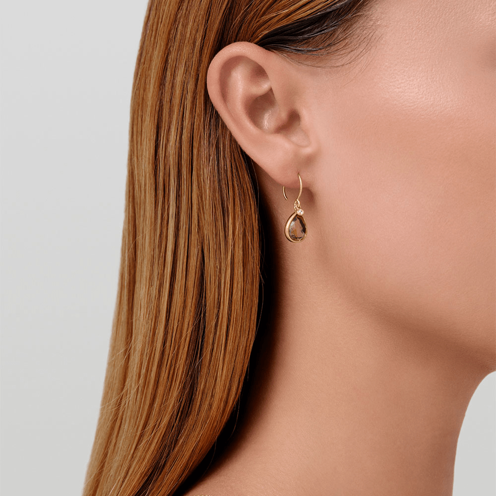 Model bærer Leela Earrings i forgyldt sølv med røget brun krystal, tæt på øret
