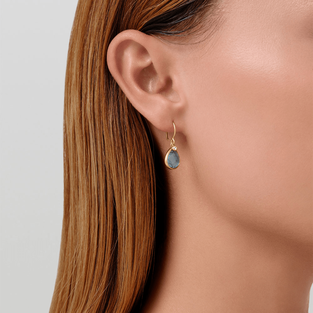 Model bærer Leela Earrings i forgyldt sølv med gråblå krystal, tæt på øret