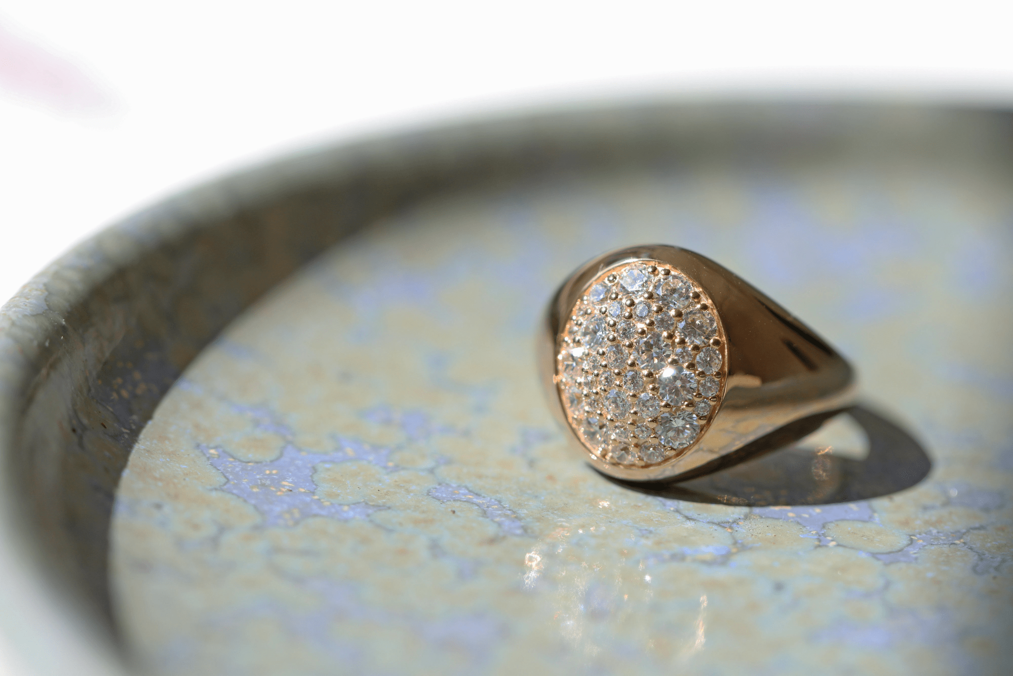 Multipave signetring fra Julie Sandlau i guld, nærbillede i keramisk skål med diamantfelt i fokus.