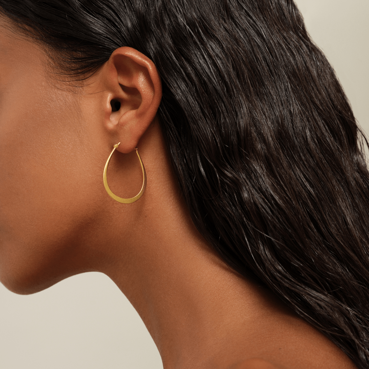 Model bærer Classic Pear Hoop øreringe i mat guld, close-up på øret