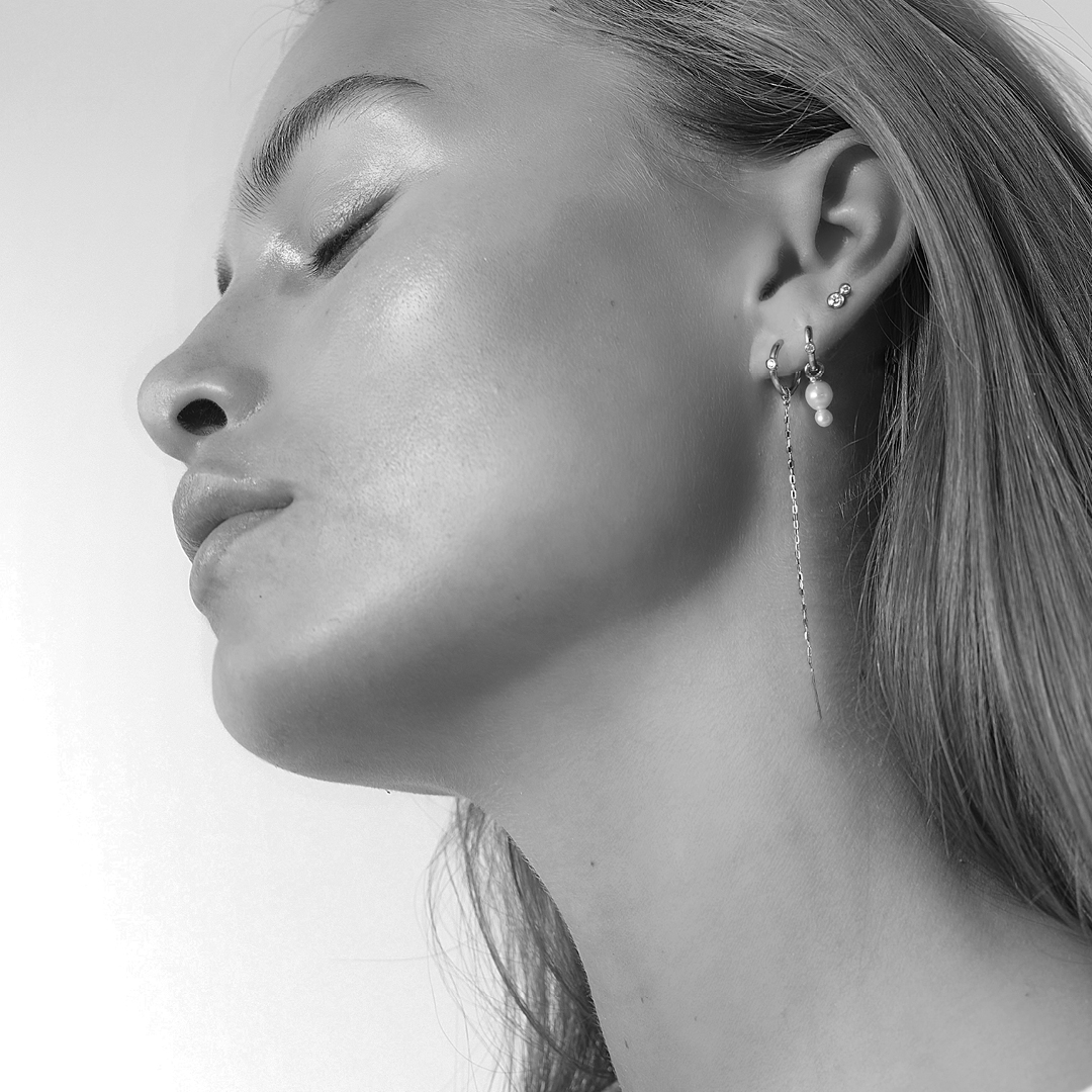 Sort-hvidt billede af model med flere øreringe i øret, herunder perlebesat creol og diamantstik fra Purity Medium and Eden Look