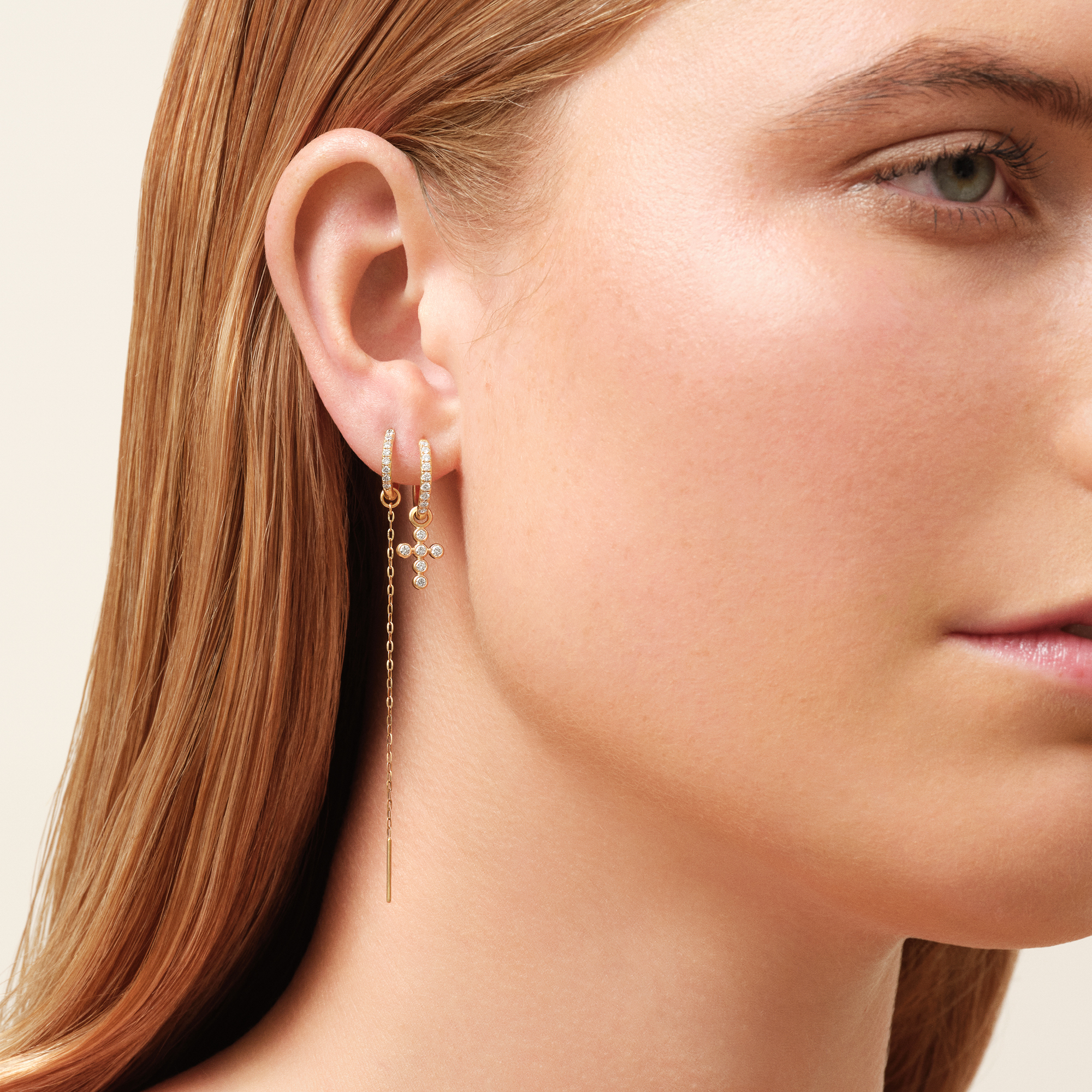 Model iført Diamond Cross Ear Pendant fra Julie Sandlau kombineret med en diamantbesat hoop og en kædeørering