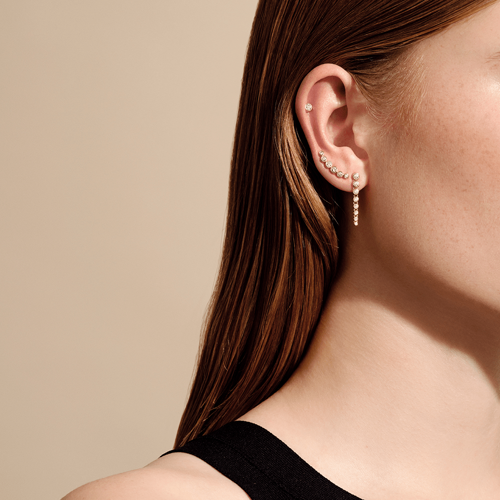 Model bærer Luster øreringen kombineret med en cartilage-stud og en kædeørering i guld