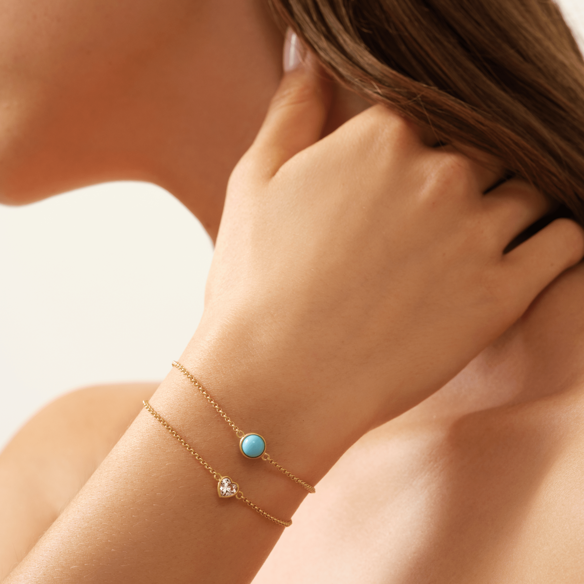 Primini armbånd med tyrkisblå cabochon-krystal båret på håndled, lagdelt med et armbånd med hjerteformet klar sten