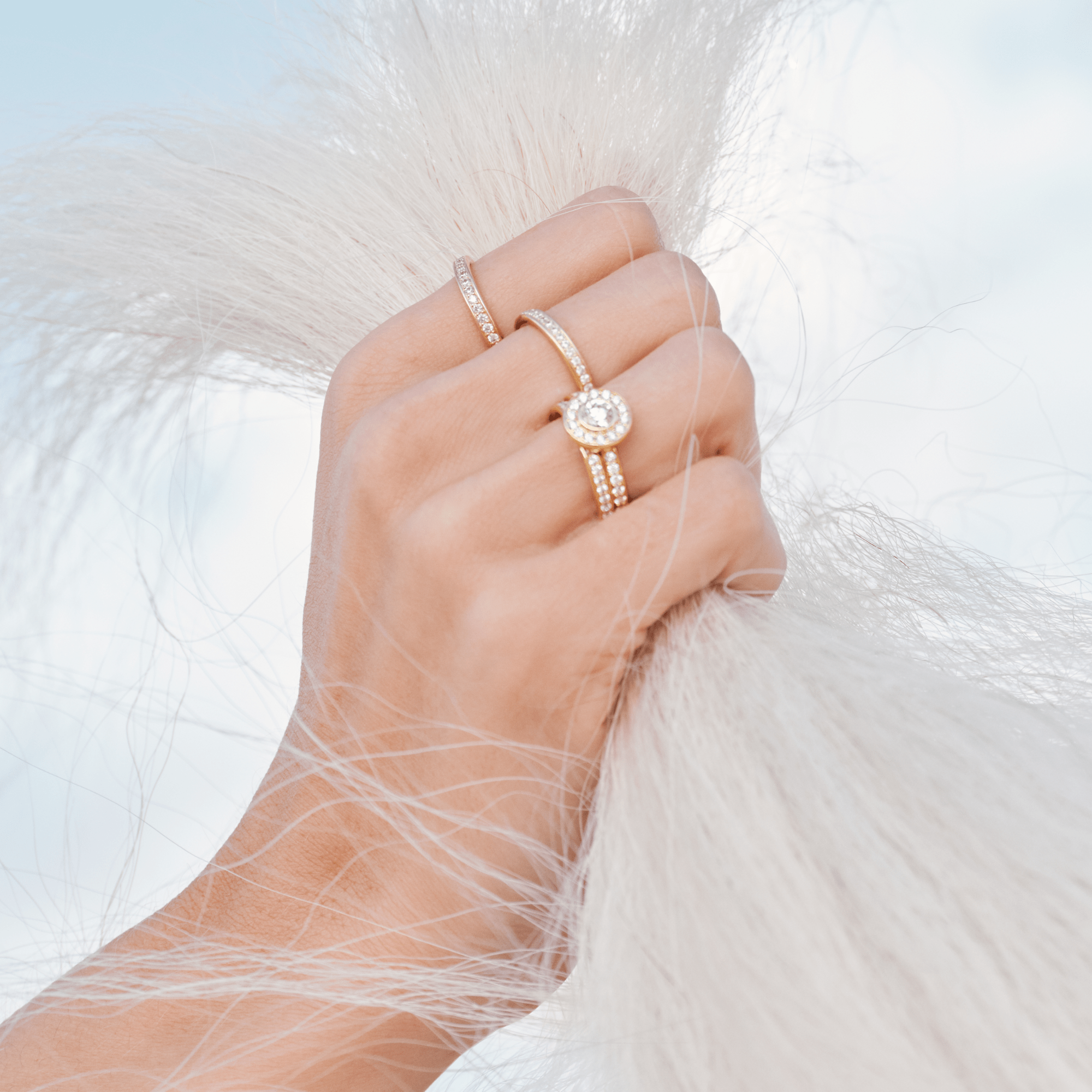 Model bærer en stack af guldringe med diamanter, herunder Heritage P.S. Ring, mens hånden holder fat i hvid pels