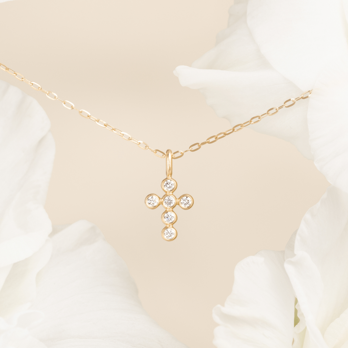 Diamantkors vedhæng i 14 karat guld med seks diamanter, close-up mellem hvide blomster