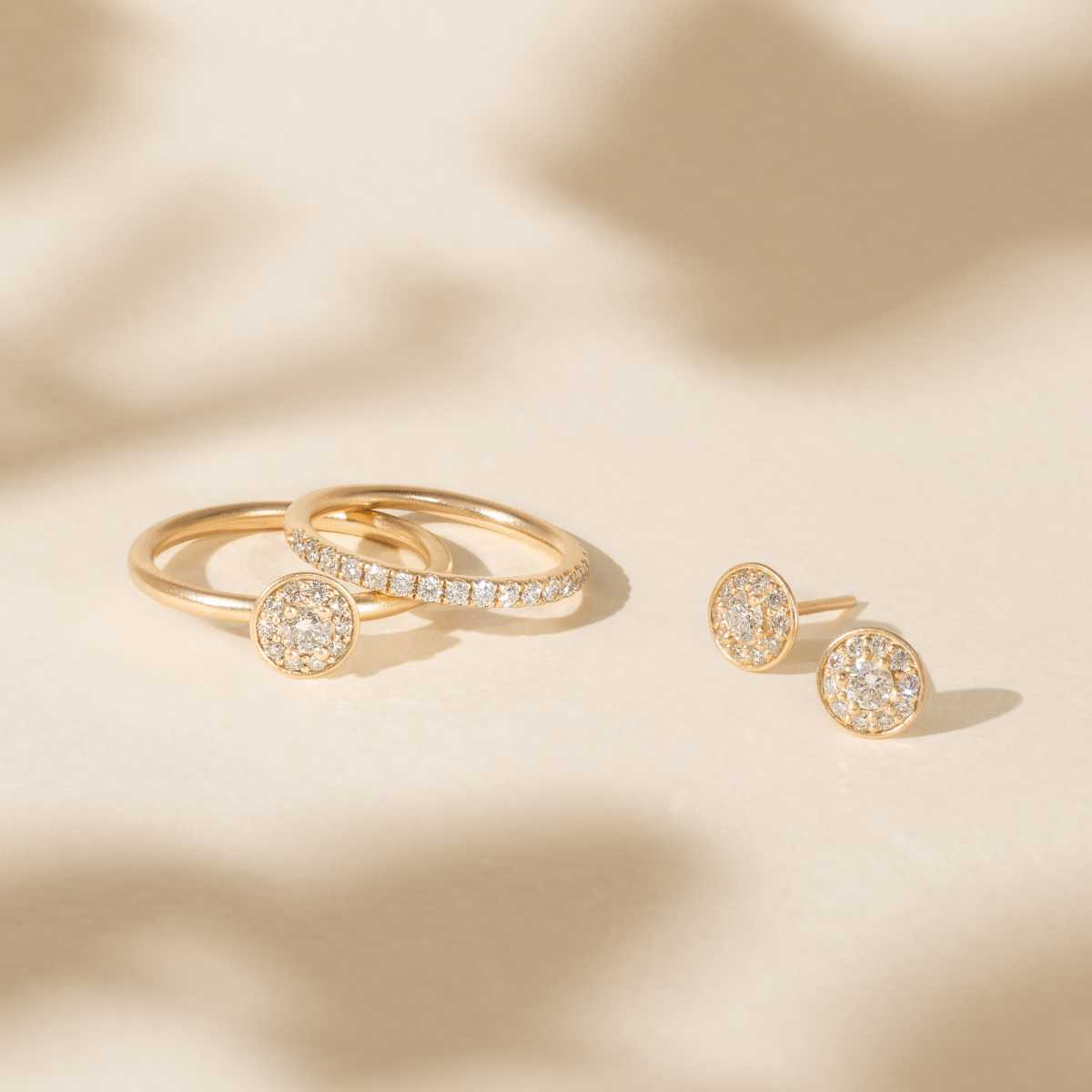 Lulia Ring stacket med halo-diamantring og et par pavé øreringe på lyst underlag